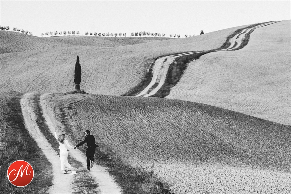 Brautpaar läuft Hand in Hand über einen Feldweg durch sanfte Hügel
