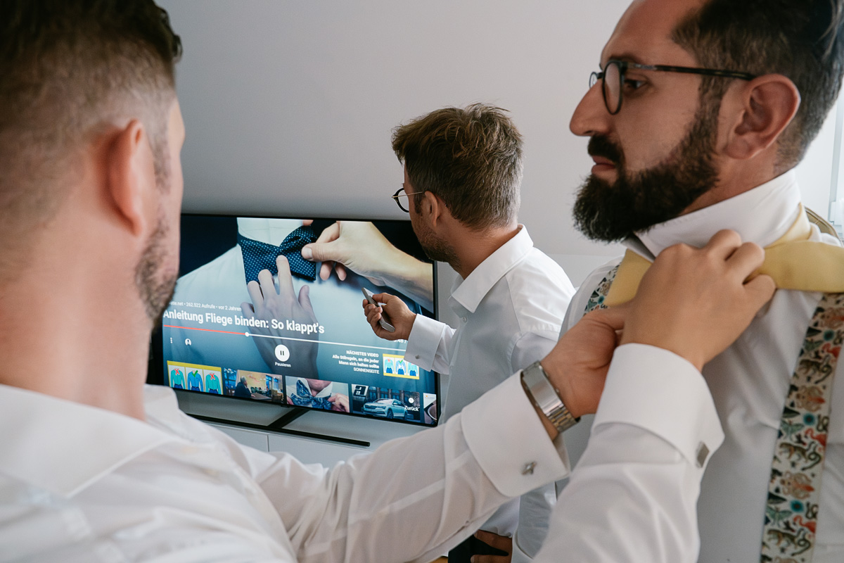 Männer binden Fliegen vor Fernseher.