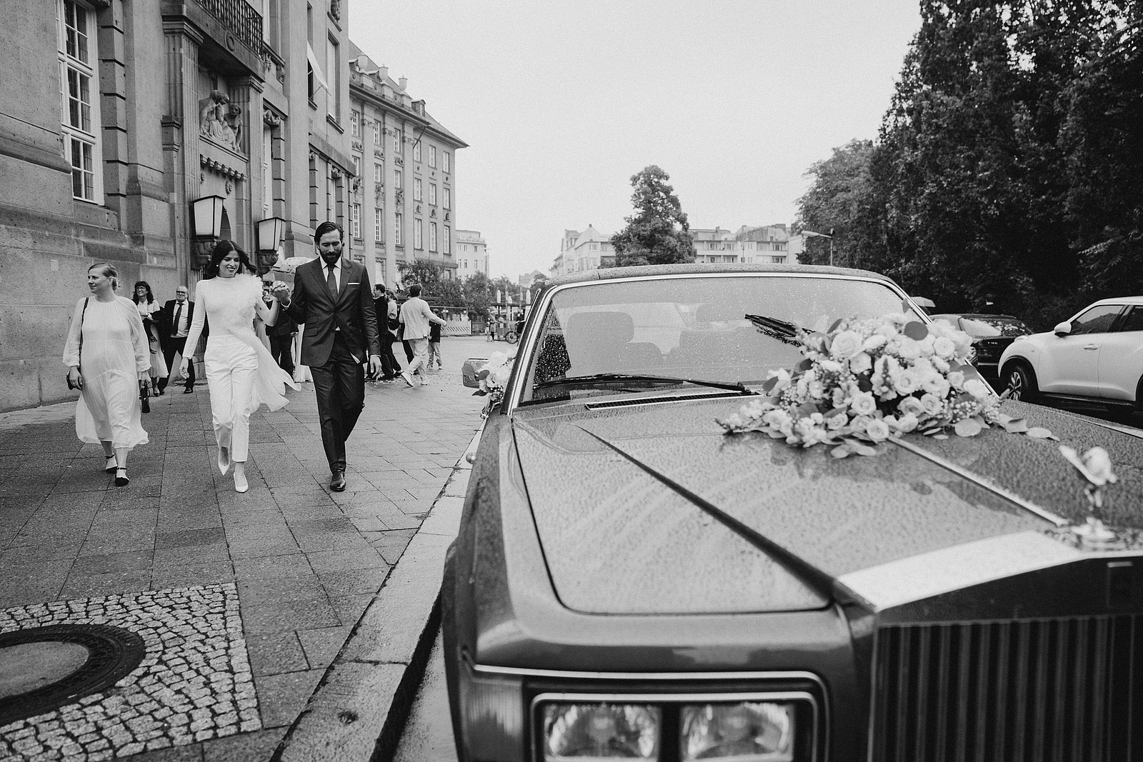 Das Brautpaar geht vor dem Rathaus Schöneberg auf das mit Blumen geschmückte Hochzeitsauto zu.