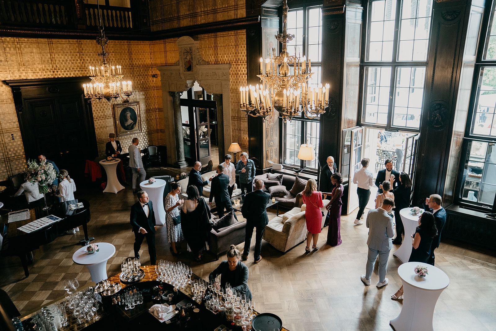 Hochzeitsgäste unterhalten sich im hohen Salon des Schlosshotels Berlin unter Kronleuchtern.