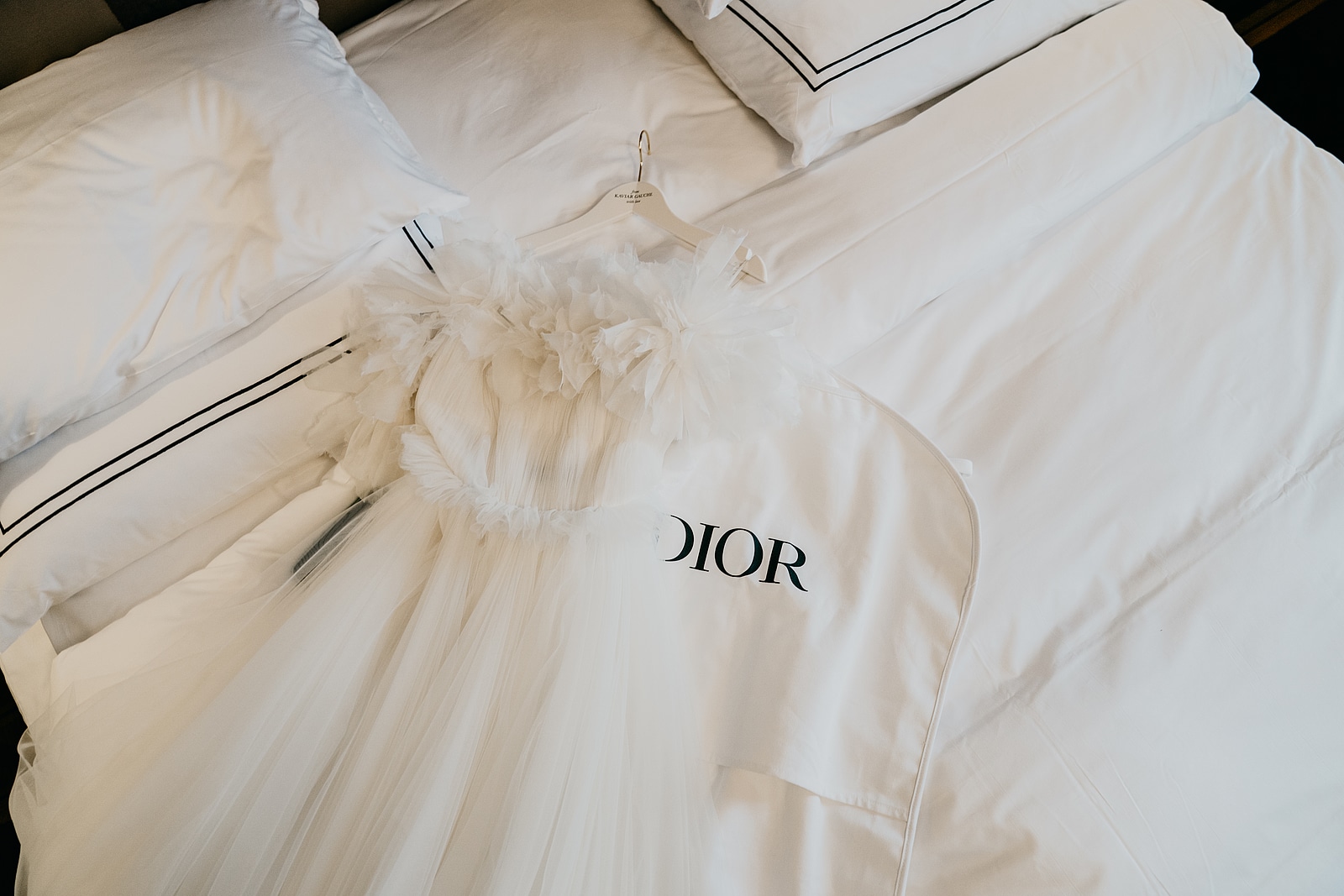 Das weiße Brautkleid mit voluminösen Rüschen liegt auf dem Bett neben einem Kleidersack.