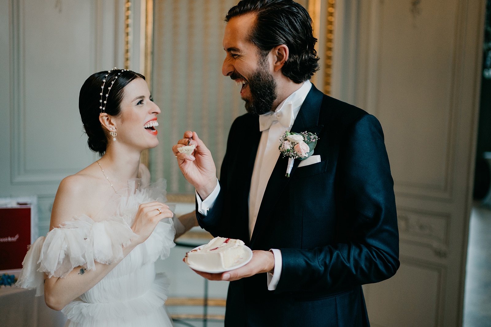 Der Bräutigam hält der lachenden Braut ein Stück Hochzeitstorte hin.