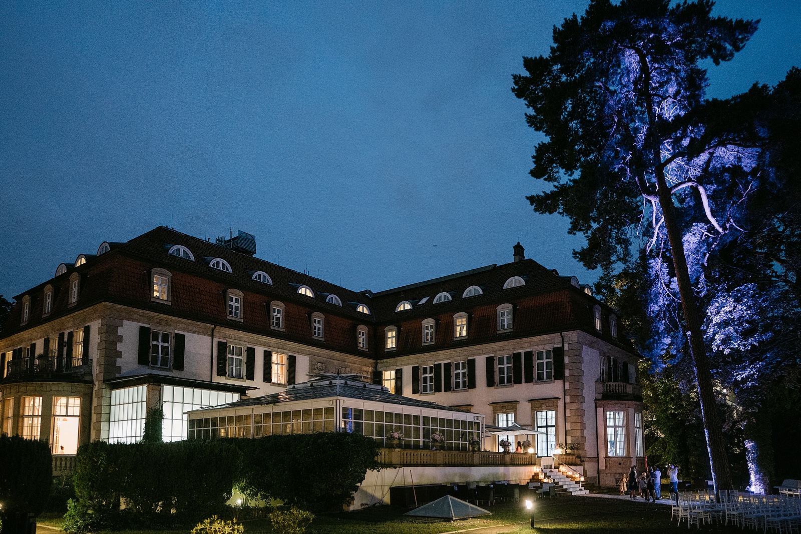 Das Schlosshotel Berlin in der Abenddämmerung mit beleuchteten Fenstern und blau angestrahltem Baum.